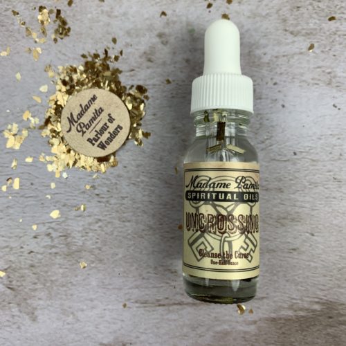 Uncrossing oil by Madame Pamita from Parlour of Wonders, featuring a small glass bottle of herbal oil on a wooden surface.