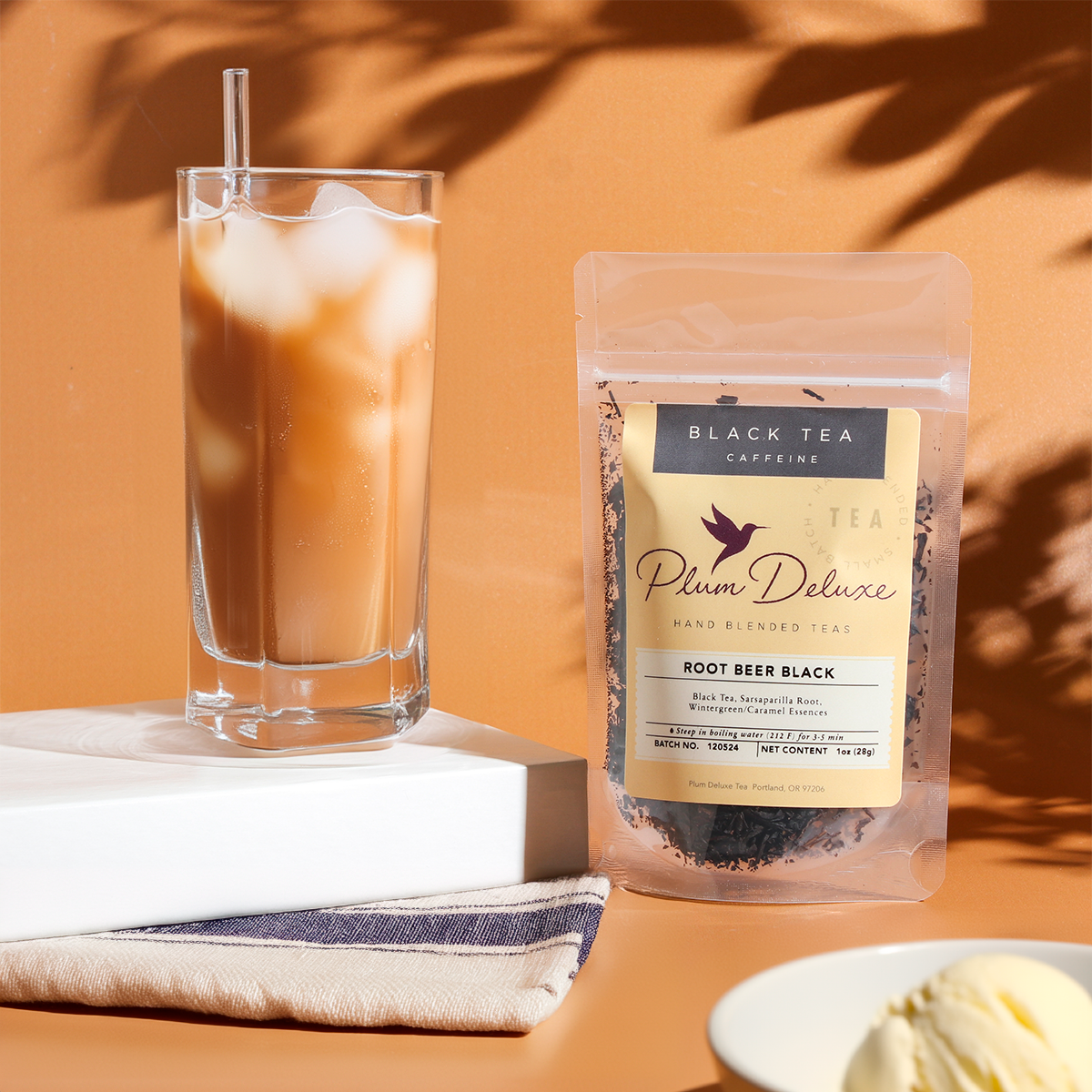 A square image of Plum Deluxe Tea's Root Beer Black Tea featuring a steaming cup of black tea with root beer flavoring and fresh ingredients.