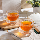 Clear glass teacup with matching saucer from Plum Deluxe Tea's Café Society collection, perfect for elegant tea service.
