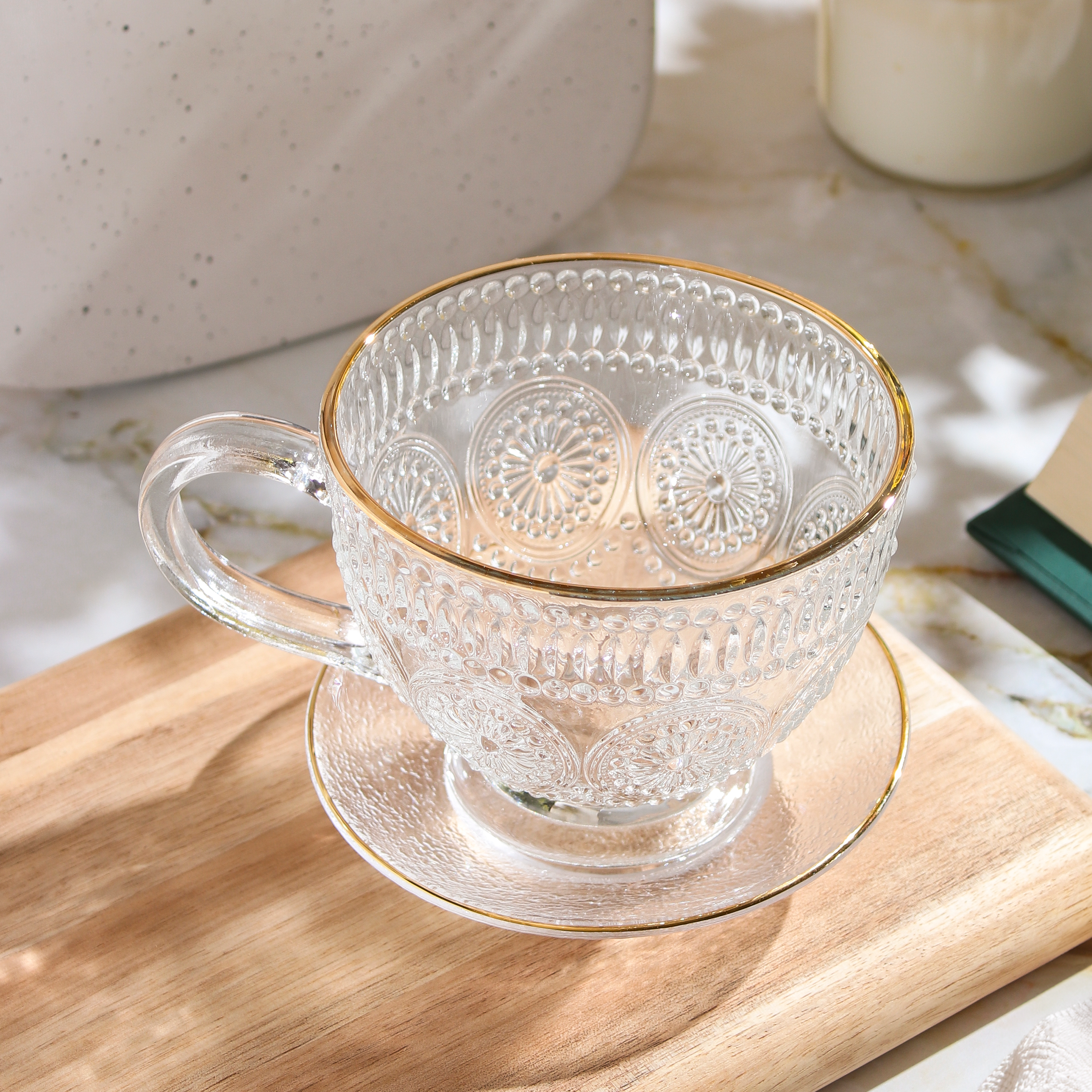 Clear glass teacup with matching saucer from Plum Deluxe Tea's Café Society collection, perfect for enjoying hot tea.