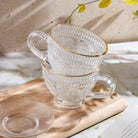Clear glass teacup with matching saucer from Plum Deluxe Tea's Café Society collection, ideal for enjoying hot tea.
