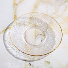 Clear glass teacup and saucer from Plum Deluxe Tea's Café Society collection, elegant and perfect for tea enjoyment.