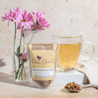 Calm Chamomile Bloom Herbal Tea by Plum Deluxe, with rose and lavender ingredients, in a clear tea infuser.