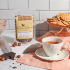 Chocolate Hazelnut Dessert Tea by Plum Deluxe Tea in a clear glass cup with brewed tea and a spoon, showcasing rich chocolate and hazelnut flavors.