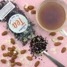 Plum Deluxe Tea Coconut Macaron Dessert Tea in a clear glass cup with a coconut macaroon on a plate, showcasing a flavorful dessert tea.