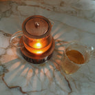 Copper Rose glass teapot with warming stand by Plum Deluxe Tea, featuring a clear glass body and elegant copper rose accents.