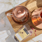 Copper Rose glass teapot with warmer from Plum Deluxe Tea, featuring a clear glass body and elegant copper rose accents.