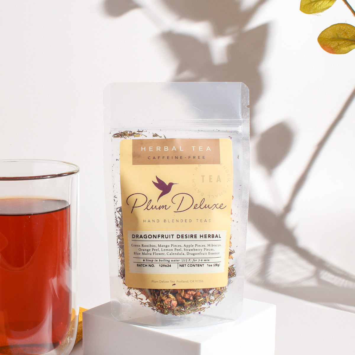 Herbal tea with vibrant pink and red dragonfruit pieces in a clear glass cup, showcasing Plum Deluxe Dragonfruit Desire Herbal Tea.