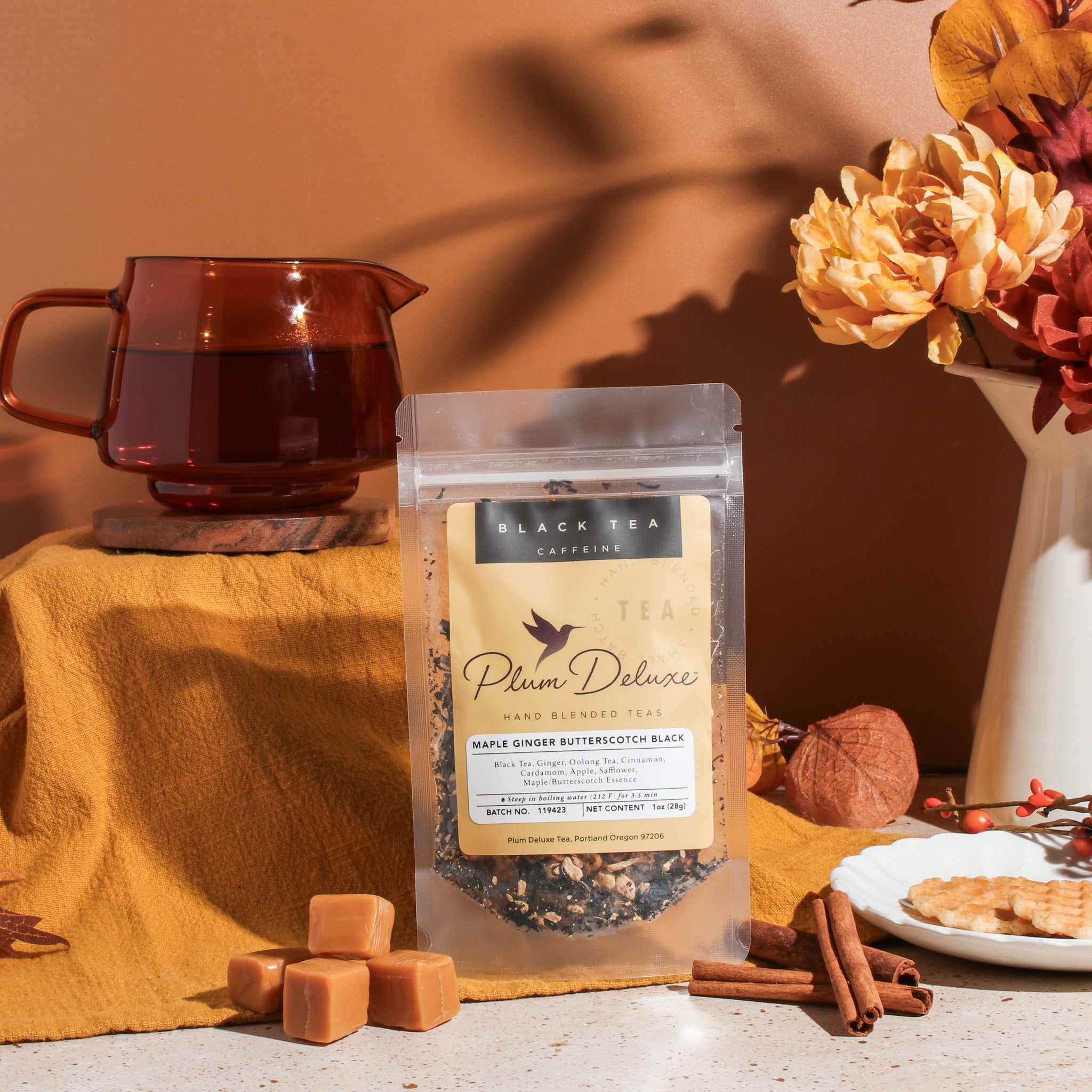 A cup of Maple Ginger Butterscotch Black Tea by Plum Deluxe Tea with tea leaves and a spoon on a rustic wooden surface.