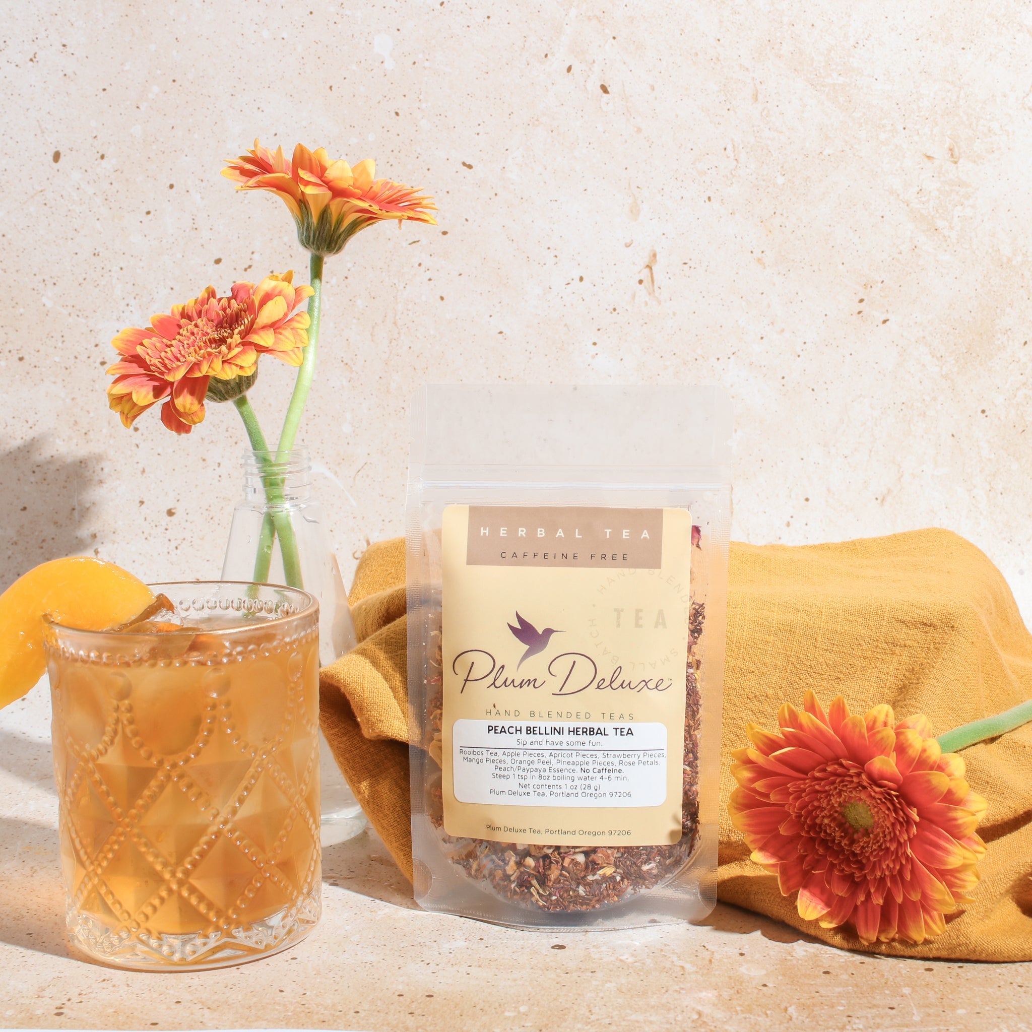 Cup of Peach Bellini Herbal Tea by Plum Deluxe, featuring a clear glass mug with brewed peach-flavored herbal tea and fresh peach slices.