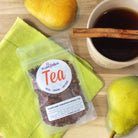 A cup of Pears and Cinnamon Herbal Tea by Plum Deluxe Tea with fresh pears and cinnamon sticks on a cozy table.