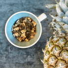 Pineapple Pop Herbal Tea by Plum Deluxe Tea in a clear glass cup showing vibrant pineapple-infused herbal tea with fresh pineapple slices