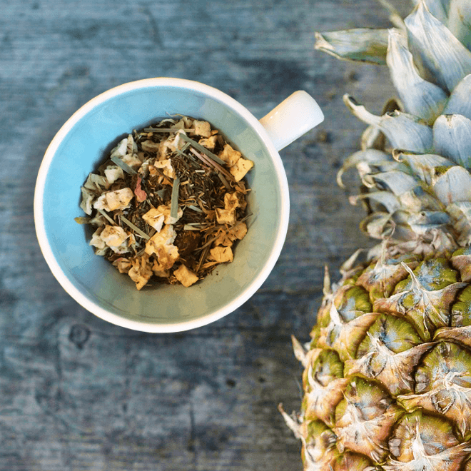 Pineapple Pop Herbal Tea by Plum Deluxe Tea in a clear glass cup showing vibrant pineapple-infused herbal tea with fresh pineapple slices