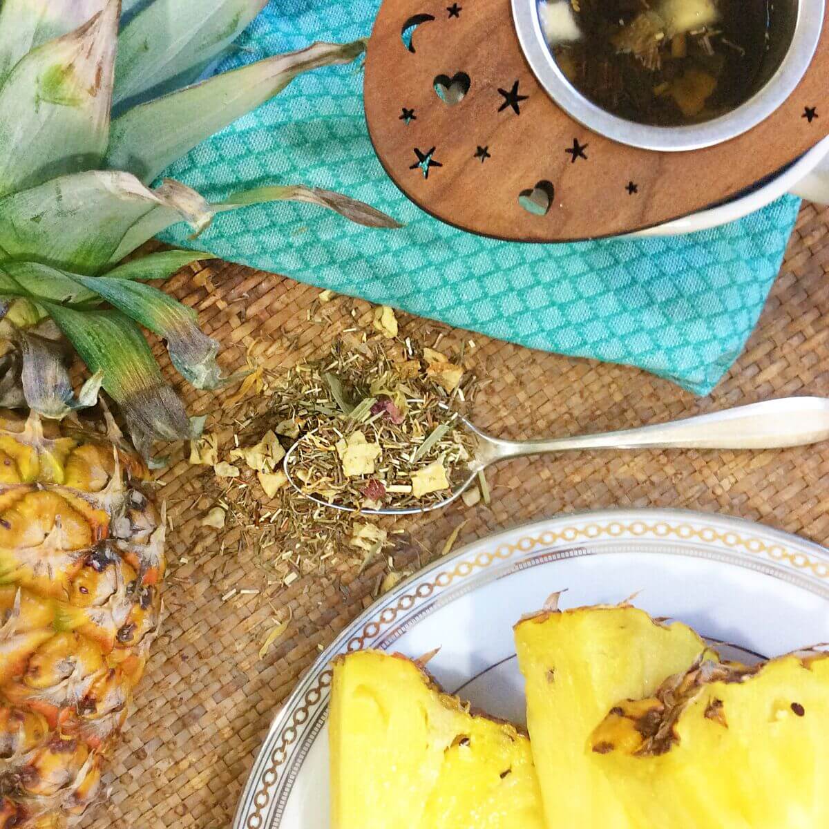 Pineapple Pop Herbal Tea by Plum Deluxe Tea in a clear glass cup with fresh pineapple slices and herbal ingredients.
