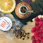 Cup of Plum Deluxe Raspberry Revitalizer Lemon Mate Tea in a glass mug with lemon slices and fresh raspberries.