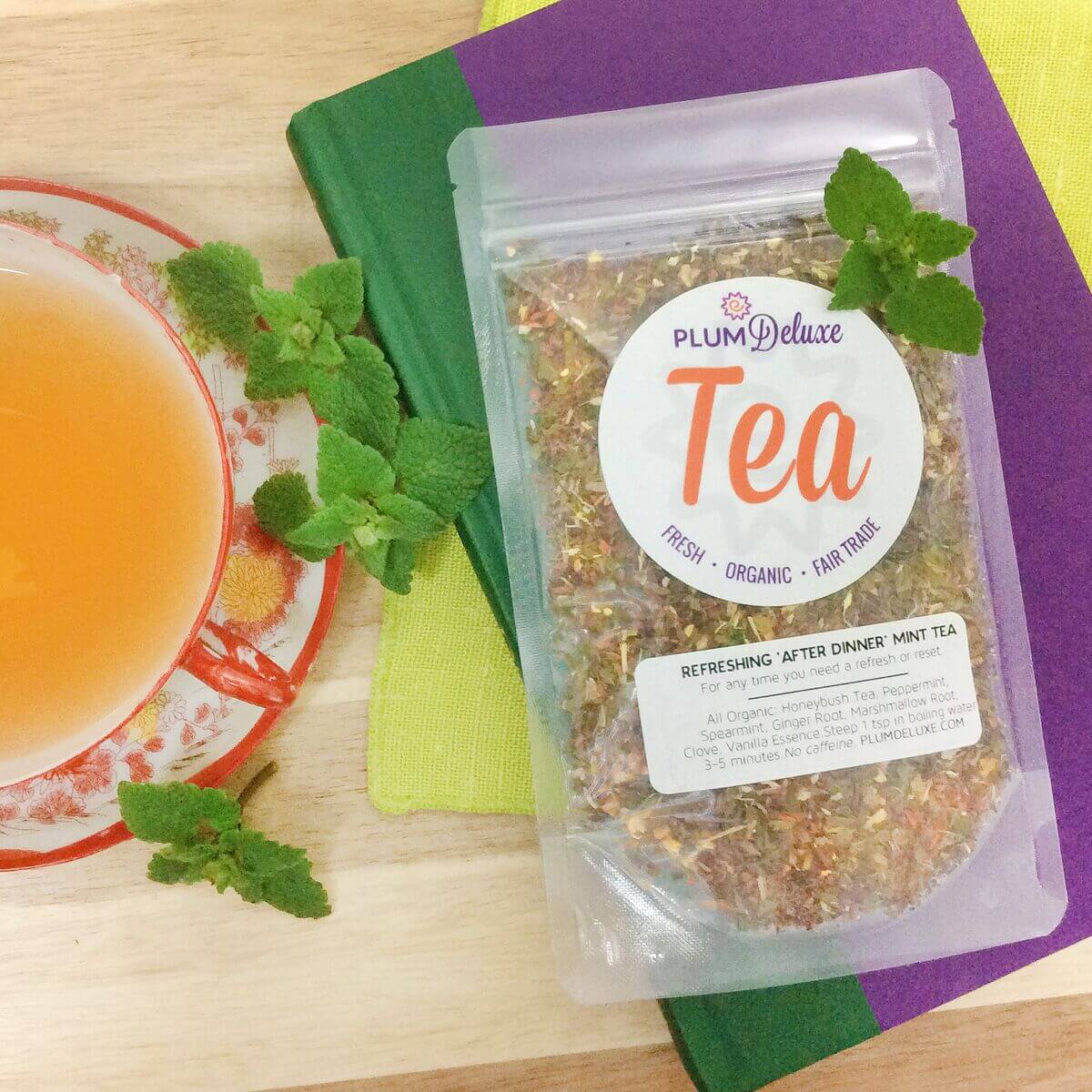 A cup of refreshing peppermint and spearmint after dinner mint tea by Plum Deluxe Tea, with fresh mint leaves and tea infuser.