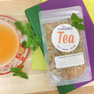A cup of refreshing peppermint and spearmint after dinner mint tea by Plum Deluxe Tea, with fresh mint leaves and tea infuser.