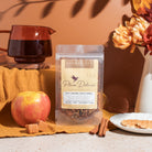 A cup of Plum Deluxe Spicy Caramel Apple Cinnamon Herbal Tea with cinnamon sticks and apple slices, steaming and ready to enjoy.
