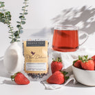 Plum Deluxe Strawberries & Cream Black Tea with Rose in a clear glass cup, showcasing brewed tea with fresh strawberry slices and rose petals.