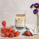 Bottle of Plum Deluxe Strawberry Immunity Herbal Tea featuring berries and echinacea, displayed in a natural setting with tea leaves.