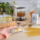Plum Deluxe Tea Ultimate Hot Tea Bundle with assorted teas, sweets, scoop, tin, and tea maker on a cozy table