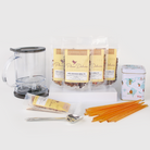 Plum Deluxe Tea Ultimate Hot Tea Bundle with assorted teas, sweets, scoop, tin, and tea maker arranged on a wooden surface.