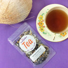 A cup of Plum Deluxe Uplifting Coconut Chai tea with coconut flakes and chai spices in a white mug on a wooden table.