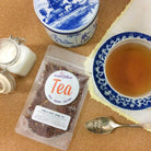 A cup of Vanilla Creme Herbal Tea by Plum Deluxe Tea with vanilla beans and herbal ingredients on a wooden table.
