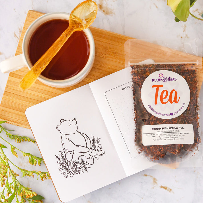 Plum Deluxe Tea Hunnybush Herbal Tea in a clear glass cup, showcasing the herbal tea's golden color and fresh herbs inside.