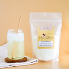 Plum Deluxe Tea Deluxe Lemonade Mix in a container with lemon slices and mix powder on a wooden table.