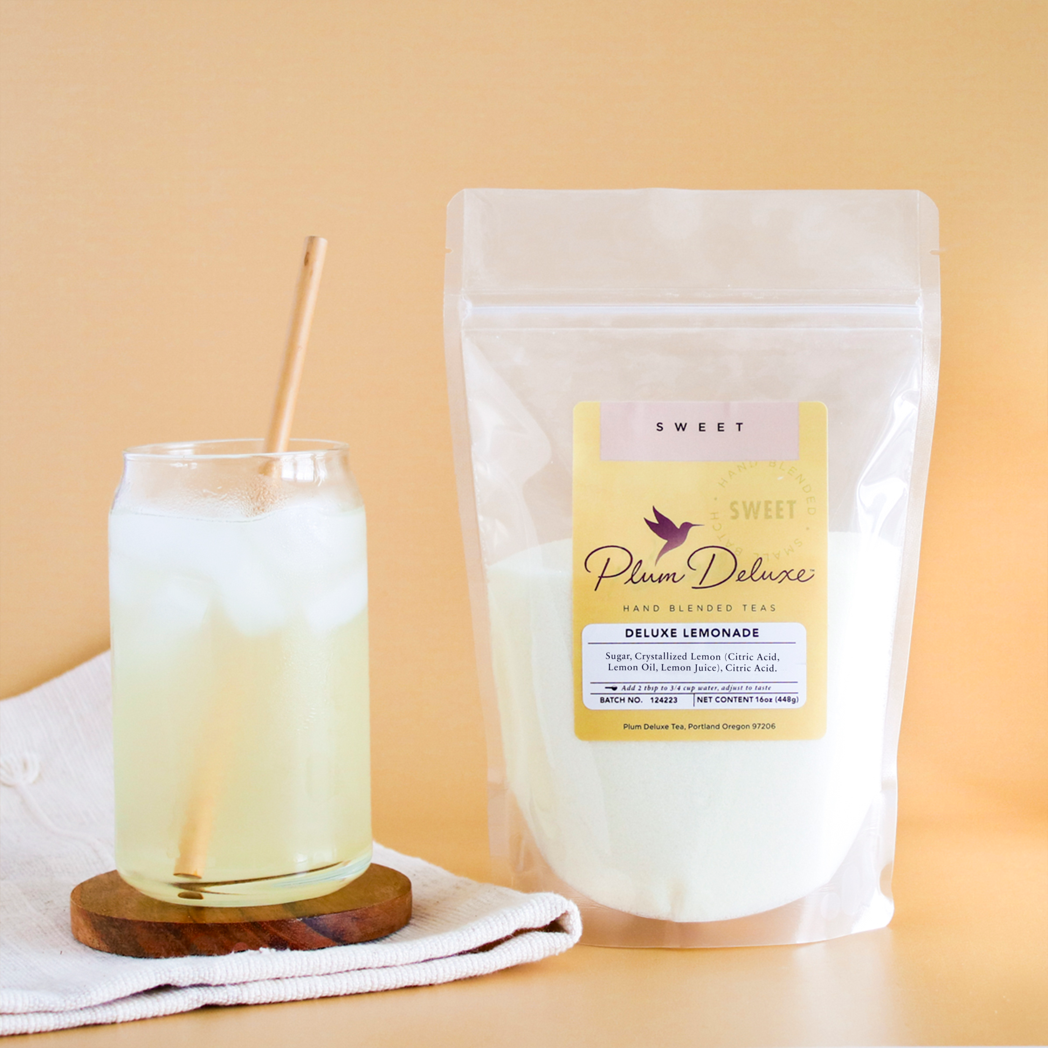 Plum Deluxe Tea Deluxe Lemonade Mix in a container with lemon slices and mix powder on a wooden table.