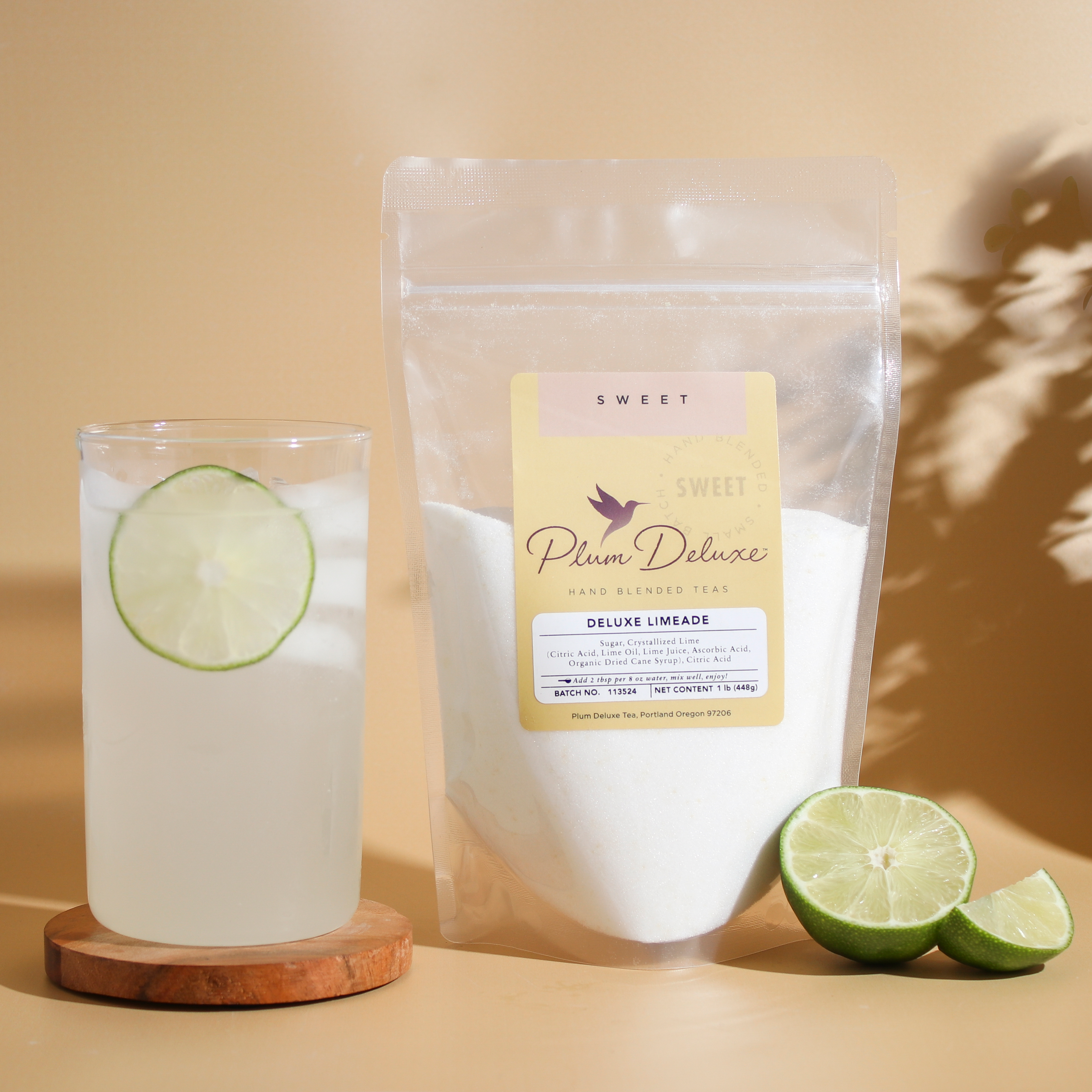 Plum Deluxe Tea Deluxe Lemonade Mix in a clear container with lemon slices and the mix packet on a wooden table.