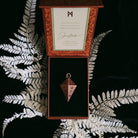 Green Glyphs Pendulum by Prisma Visions, featuring a detailed green and gold design, hanging from a chain.