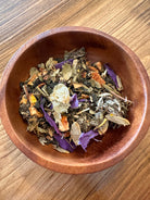 Cup of Moon Magic Herbal Tea by Sage & Stone Apothecary with dried herbs and moon-themed packaging in the background.