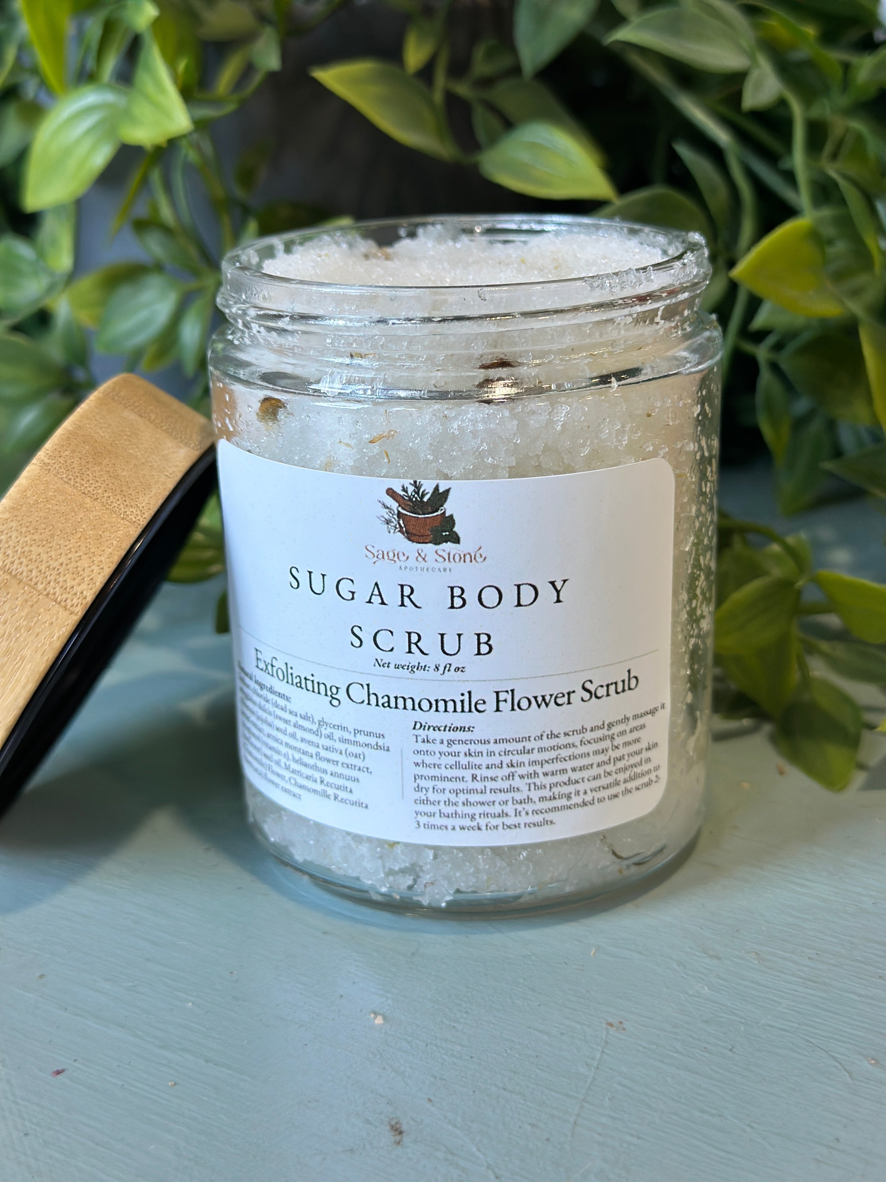 Exfoliating chamomile flower scrub in a jar from Sage & Stone Apothecary, showing the natural textured scrub with chamomile flowers.