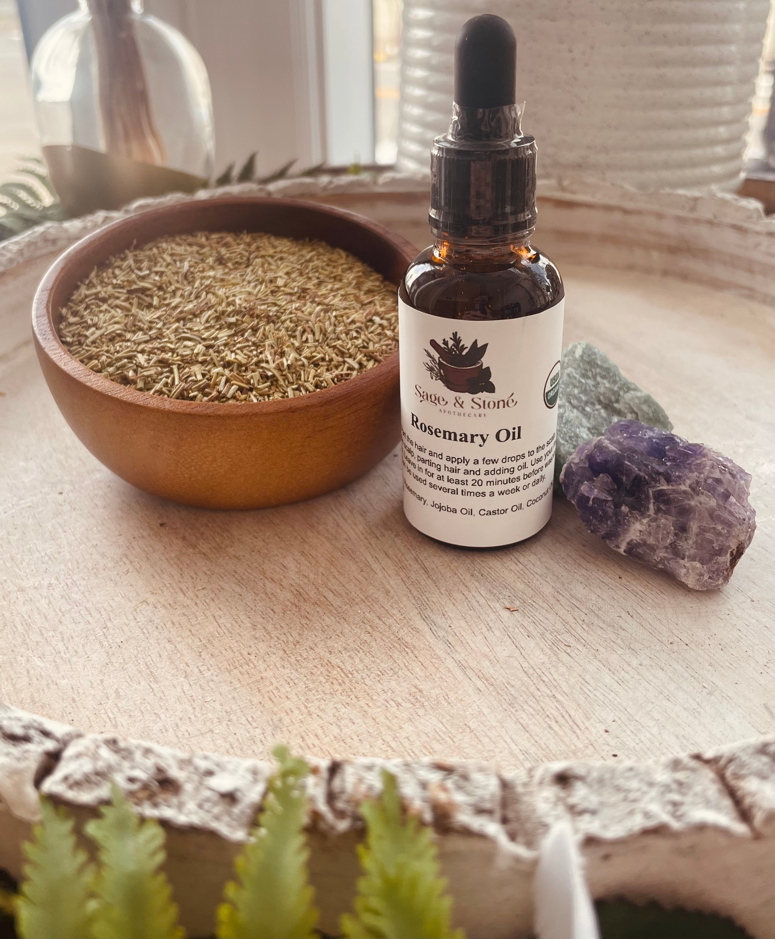 Sage & Stone Apothecary rosemary oil bottle for body care and wellness, with fresh rosemary sprigs around it.