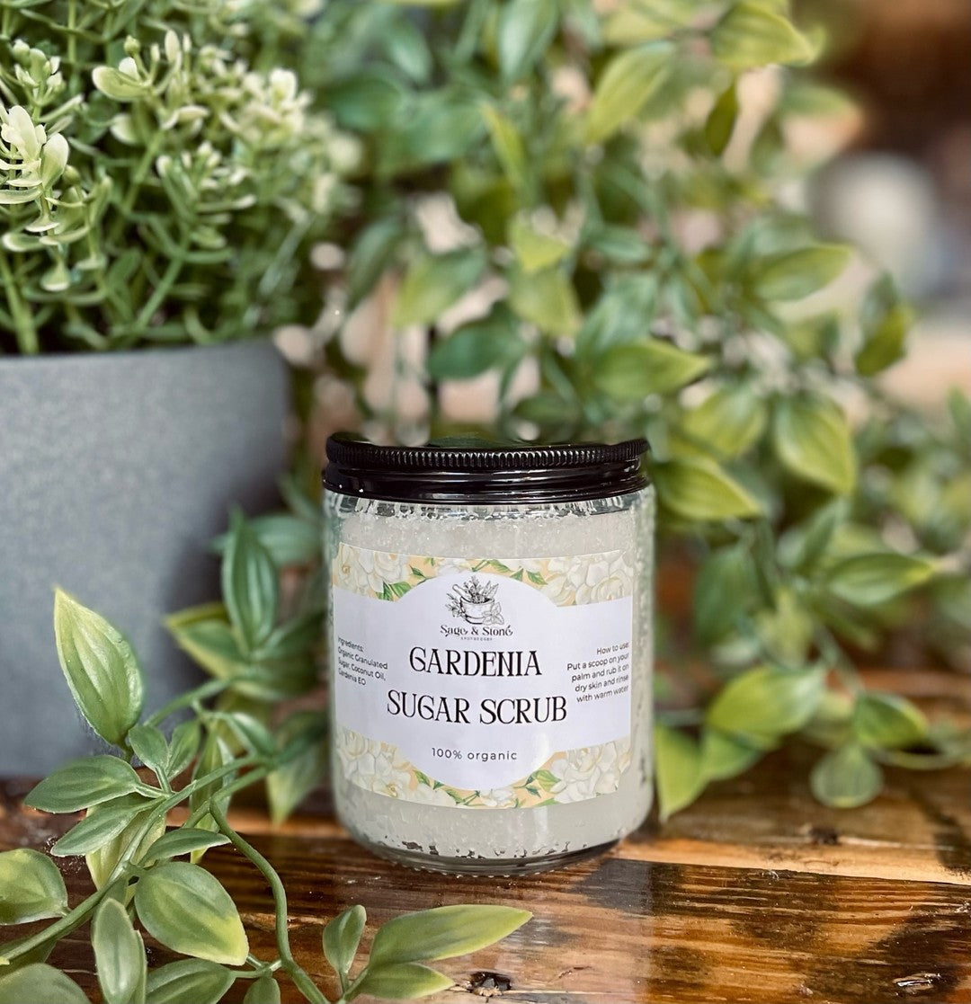 Sage & Stone Apothecary Gardenia Sugar Scrub in a jar with fresh gardenia flowers, showcasing a natural personal care product.
