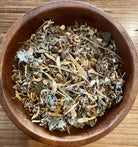 Cup of Sage & Stone Apothecary anti-nausea herbal tea with fresh herbs and tea leaves in a rustic setting.