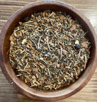 Sage & Stone Apothecary anti-inflammation herbal tea in a clear glass cup with fresh herbs and tea leaves on a wooden surface.