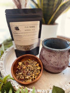 A cup of Sage & Stone Apothecary Cold Defender tea with fresh herbs and lemon slices on a rustic wooden table.