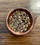 A cup of Cold Defender herbal tea from Sage & Stone Apothecary with fresh herbs and lemon slices on a wooden table.