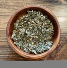 Sage & Stone Apothecary Happy Hormone Balance Tea in a glass cup with dried herbs and flowers, promoting hormonal wellness.