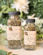 Sage & Stone Apothecary Liver Detox Blend tea in a glass cup with herbal tea leaves and a wooden spoon on a white background.