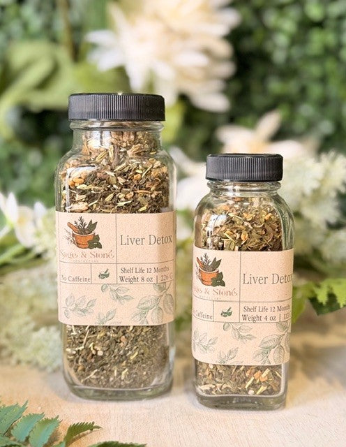 Sage & Stone Apothecary Liver Detox Blend tea in a glass cup with herbal tea leaves and a wooden spoon on a white background.