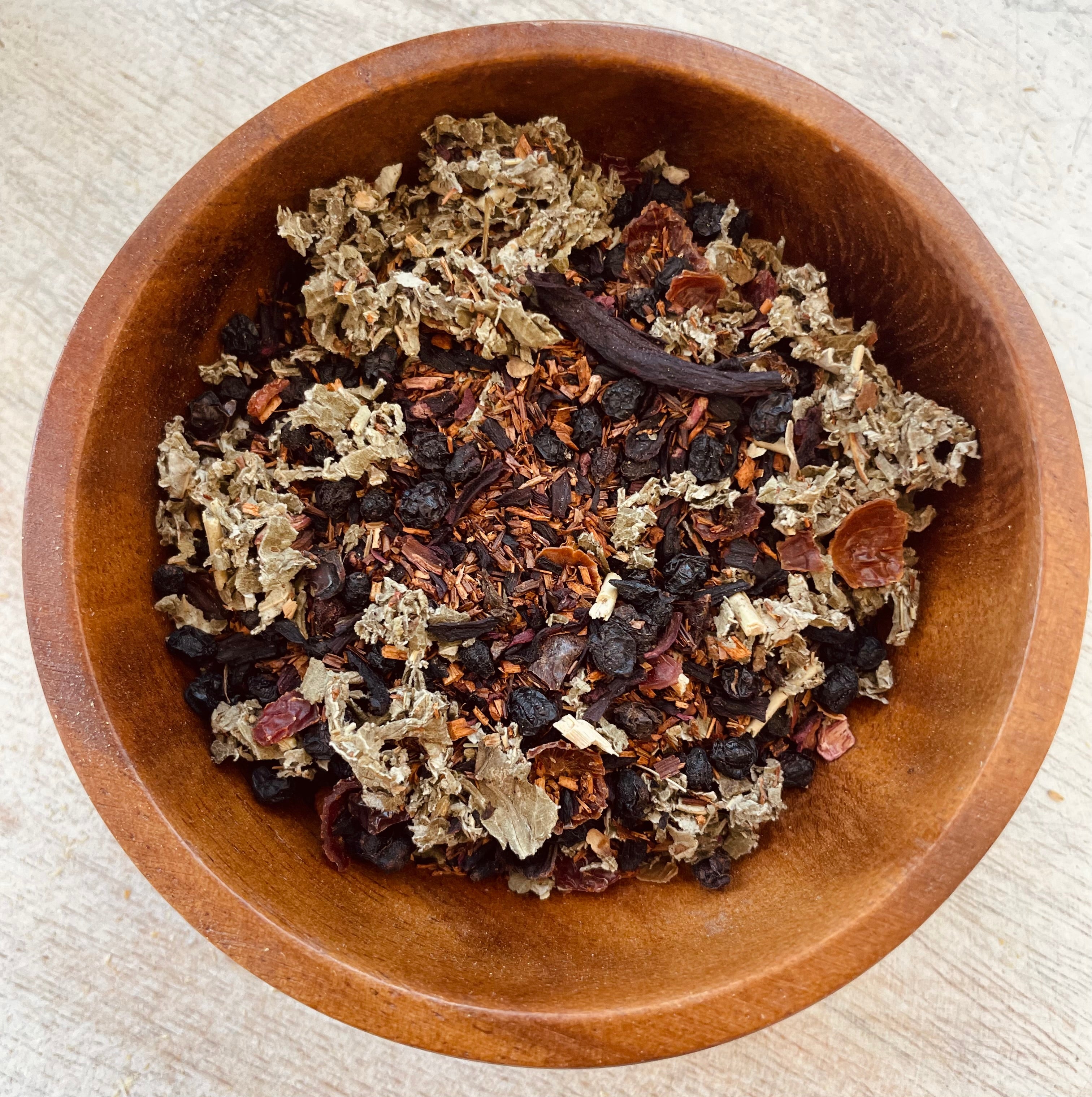 Herbal tea in a glass mug labeled Love Spell by Sage & Stone Apothecary, with dried herbs and tea leaves visible.