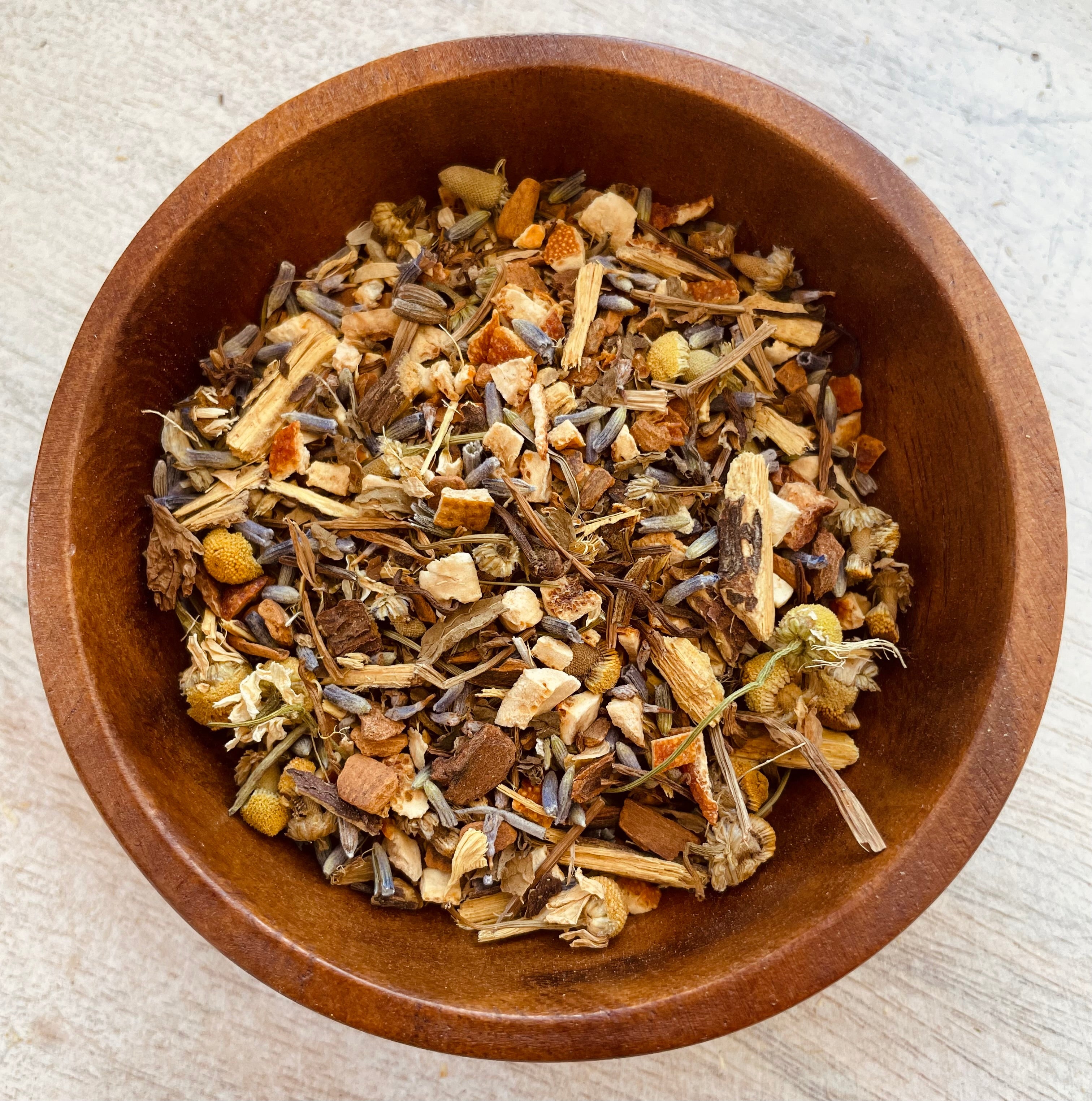 A cup of Sleepy Blend herbal tea by Sage & Stone Apothecary, filled with calming herbal tea leaves and flowers on a wooden surface.