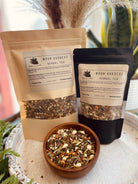 Herbal tea named Moon Goddess by Sage & Stone Apothecary, featuring a steaming cup with moon and floral motifs on a rustic wooden table.
