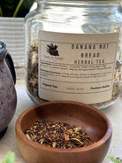 Sage & Stone Apothecary banana nut bread flavored tea in a cozy cup, with banana slices and nuts beside it.