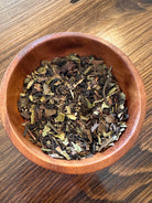 Sage & Stone Apothecary Flo Herbal Tea in a glass mug, showcasing a vibrant herbal blend with fresh herbs and dried flowers.