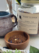 Glass Slipper Tea by Sage & Stone Apothecary in a clear glass cup with brewed tea and a tea infuser, showcasing a calming herbal blend.